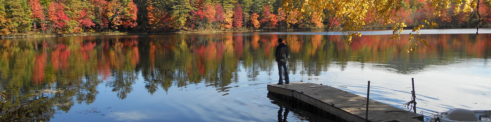 Man standing at end of dock on Lake Luzerne with fall colors