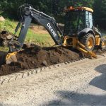 A yellow utility vehicle digging up an unpaved road during construction