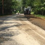 An unpaved dirt road partially worked on by a construction vehicle.