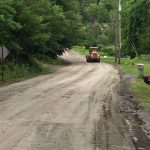 An orange tractor driving down an unpaved dirt road in the countryside